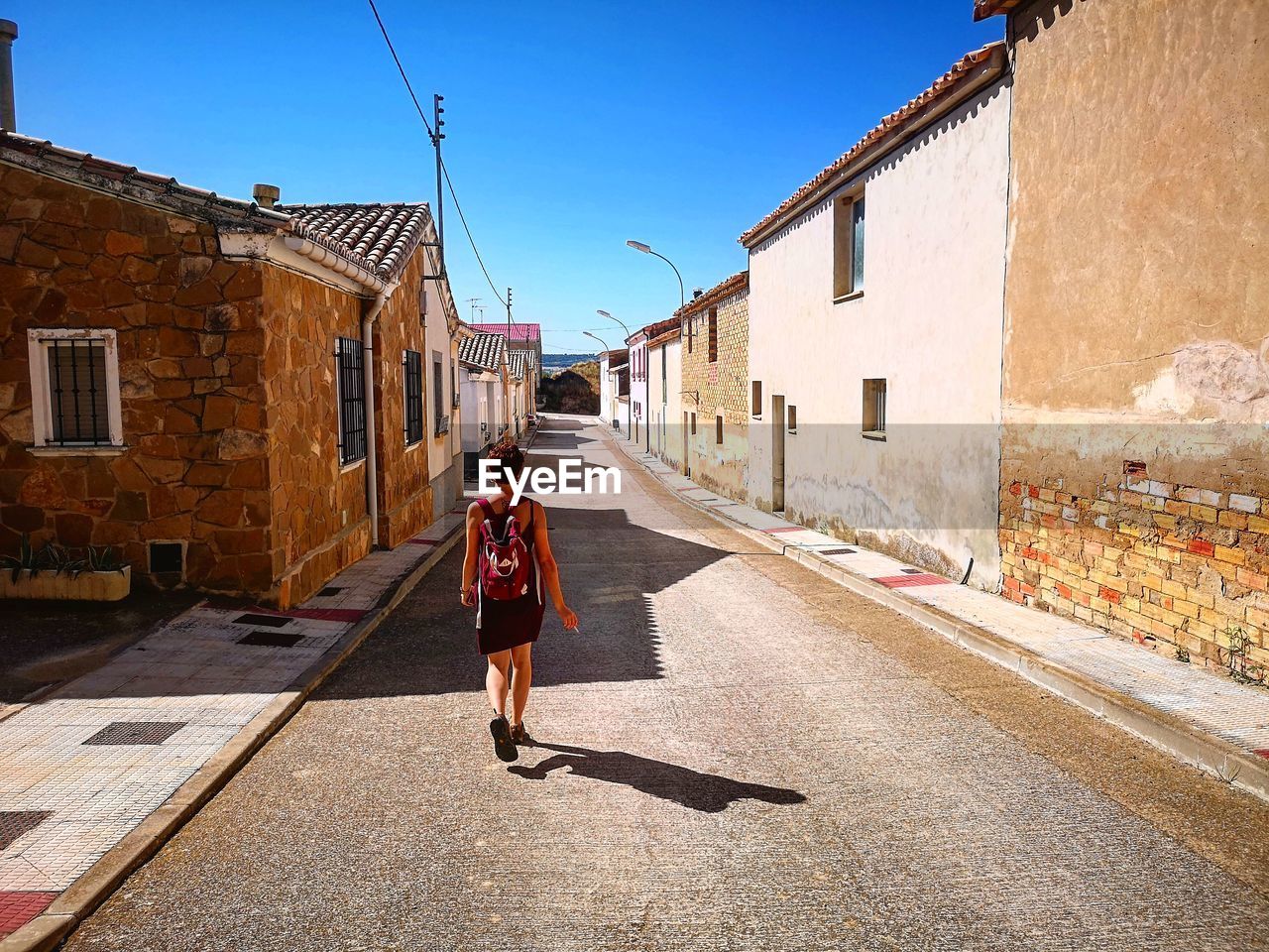 WOMAN STANDING ON FOOTPATH AMIDST BUILDINGS