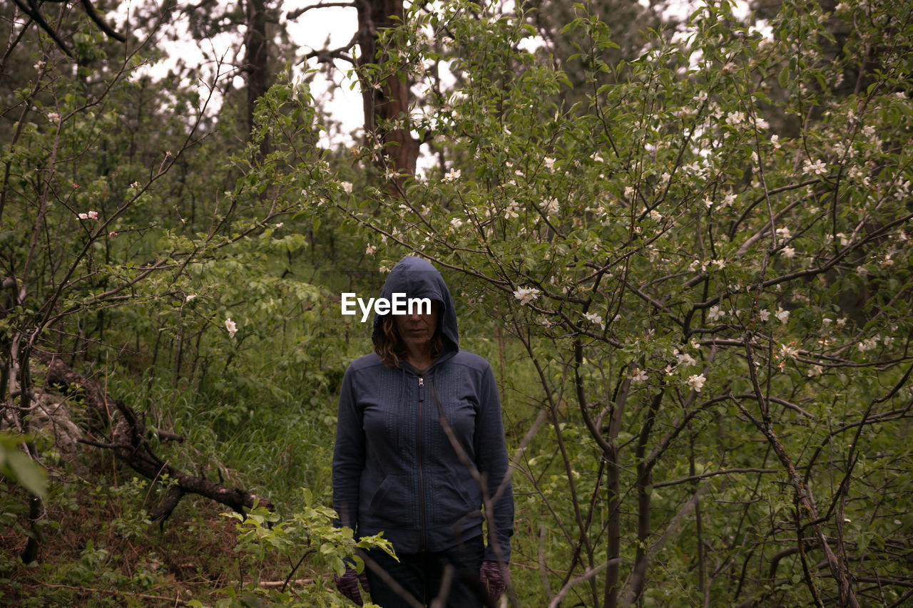 Mature woman wearing hooded shirt while standing by trees at forest