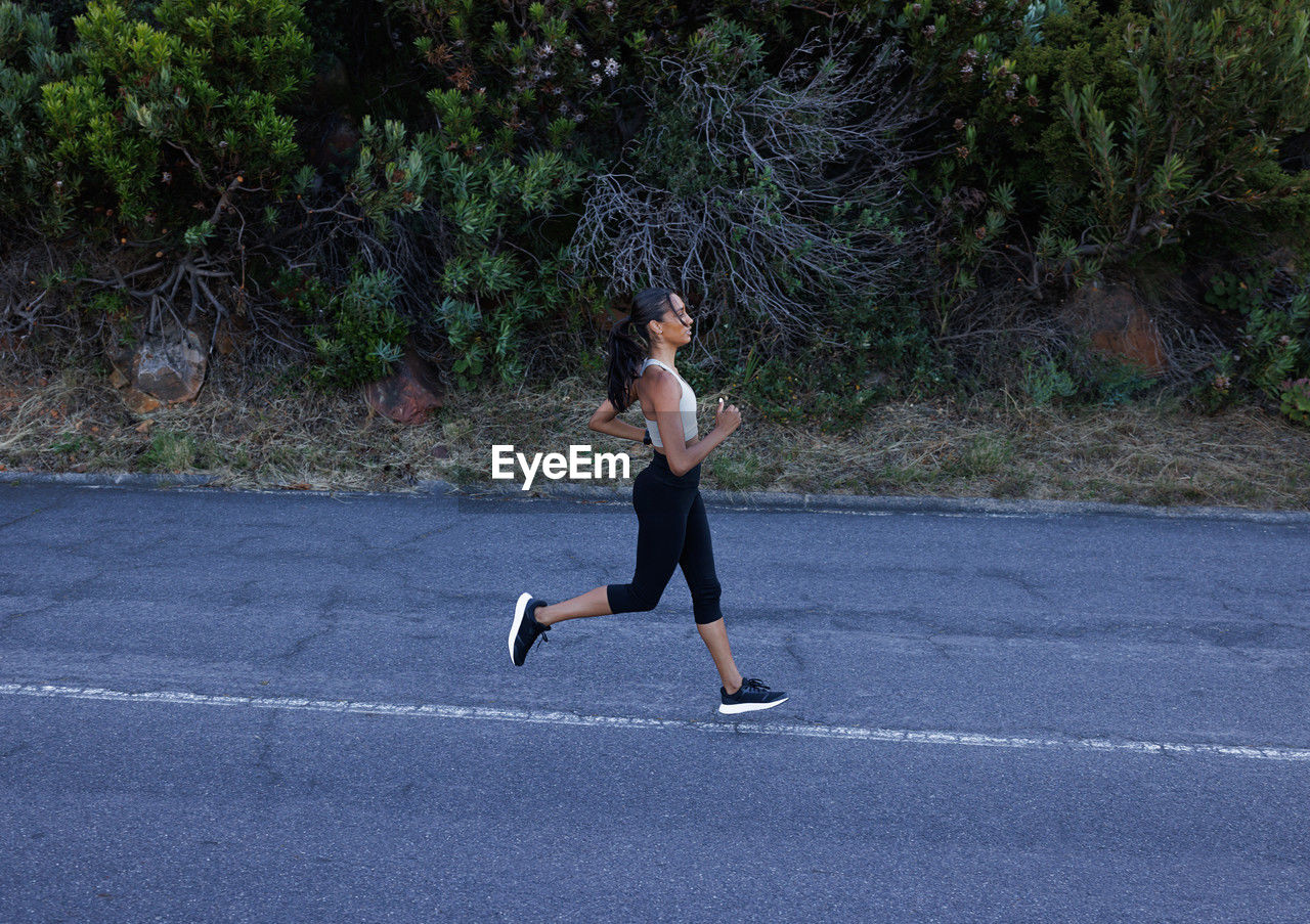 full length, one person, sports, lifestyles, exercising, sports clothing, running, adult, clothing, day, young adult, motion, road, vitality, leisure activity, jogging, side view, athlete, plant, nature, women, determination, casual clothing, tree, sports training, outdoors, athleticism, wellbeing, person, city, transportation, concentration
