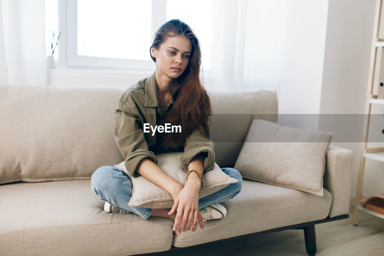 portrait of young woman using phone while sitting on sofa at home