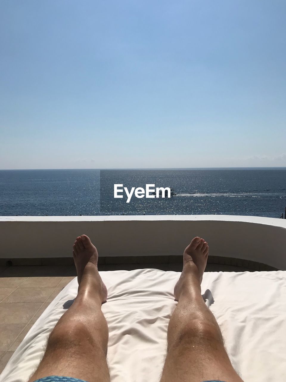 LOW SECTION OF MAN RELAXING ON SEA AGAINST SKY