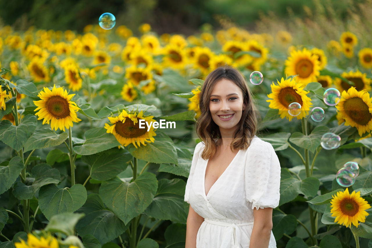 Portrait of smiling woman standing against sunflower