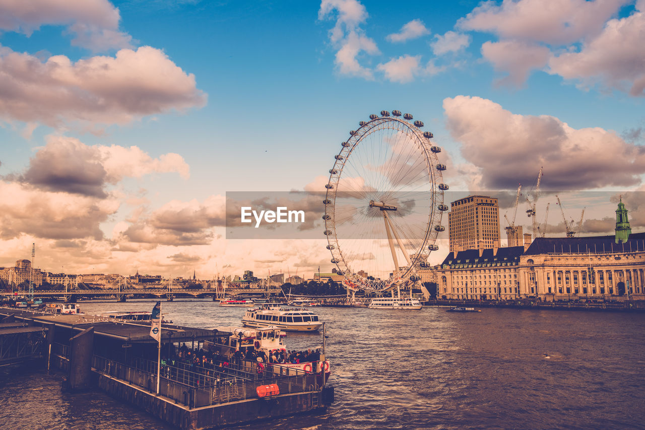 Ferris wheel in city against cloudy sky