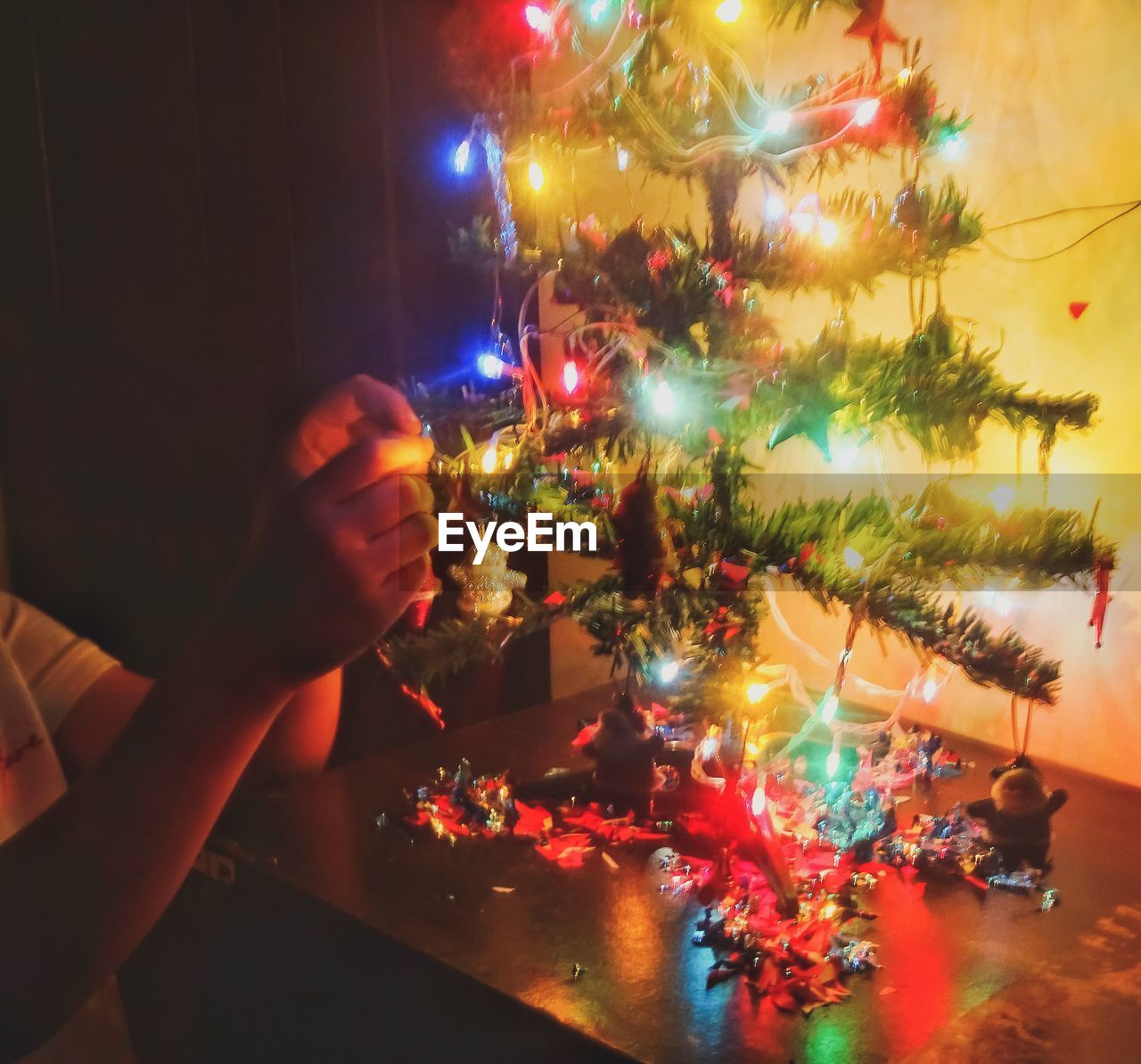 Cropped hand decorating illuminated christmas tree at home