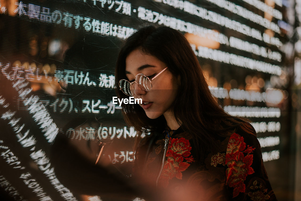 Close-up of young woman using mobile phone standing outdoors at night