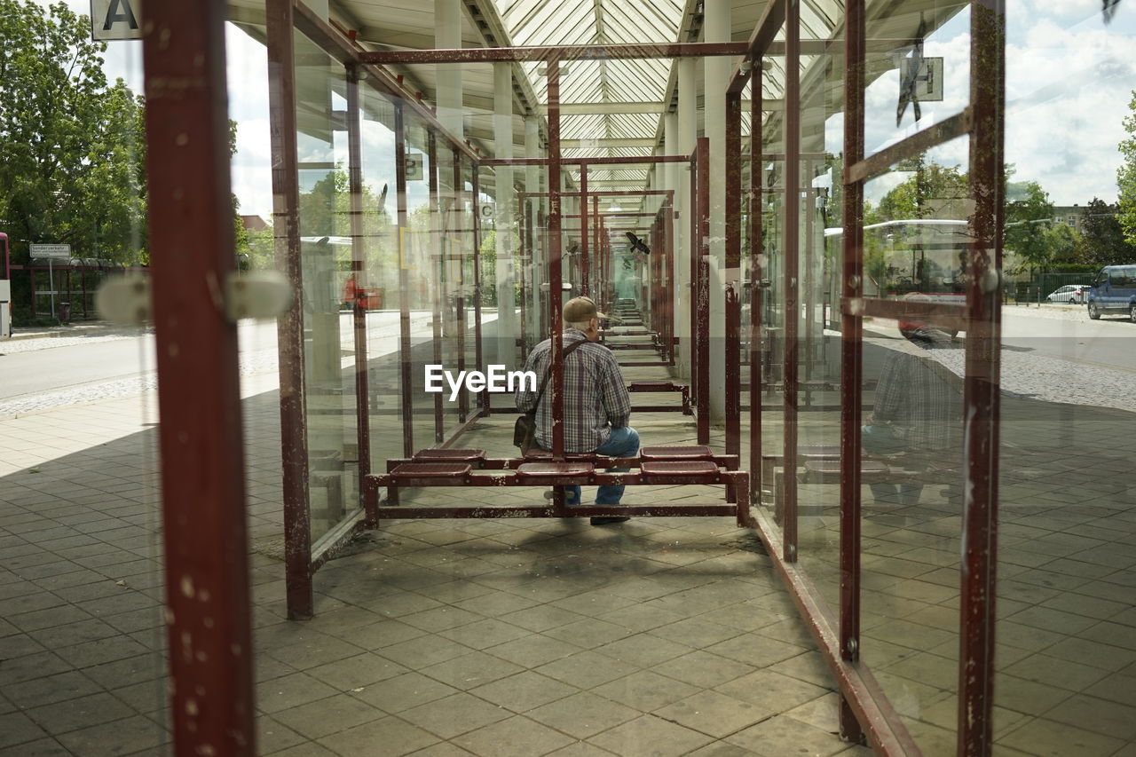 Rear view of man sitting in colonnade amidst glass windows
