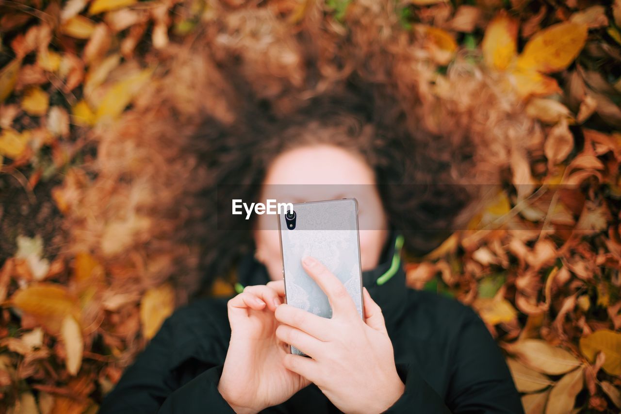 Directly above shot of woman using phone while lying on field at park