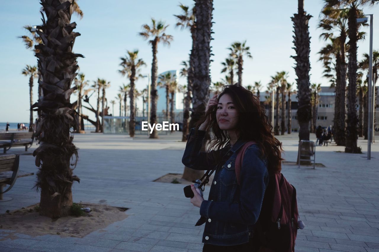 Portrait of young woman standing by palm trees