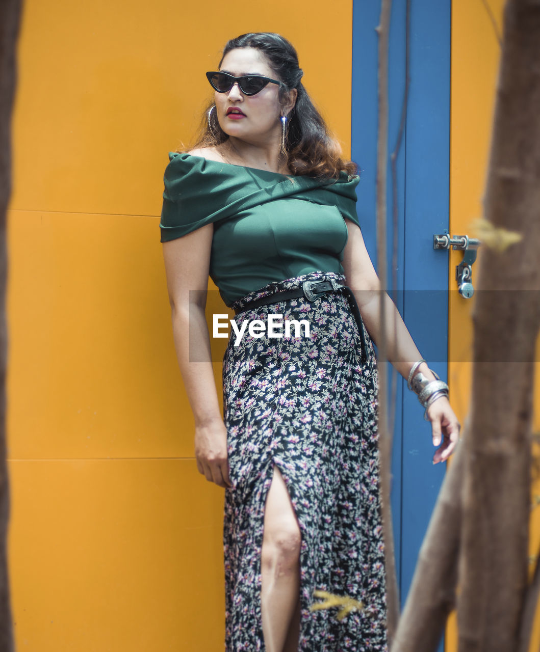 Young woman wearing sunglasses standing against yellow wall