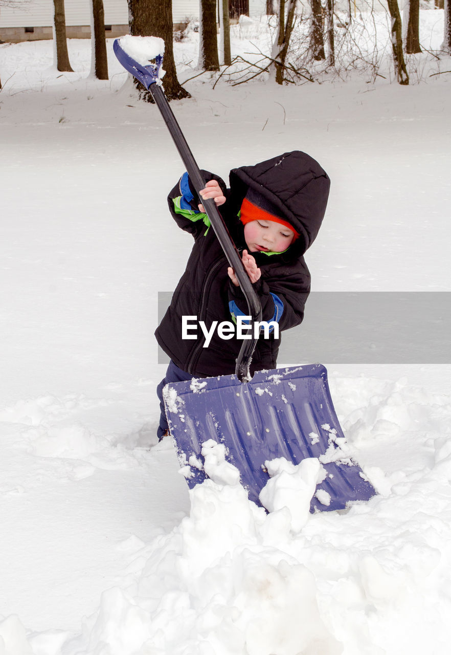 Small boy uses a big shovel to try and shovel snow