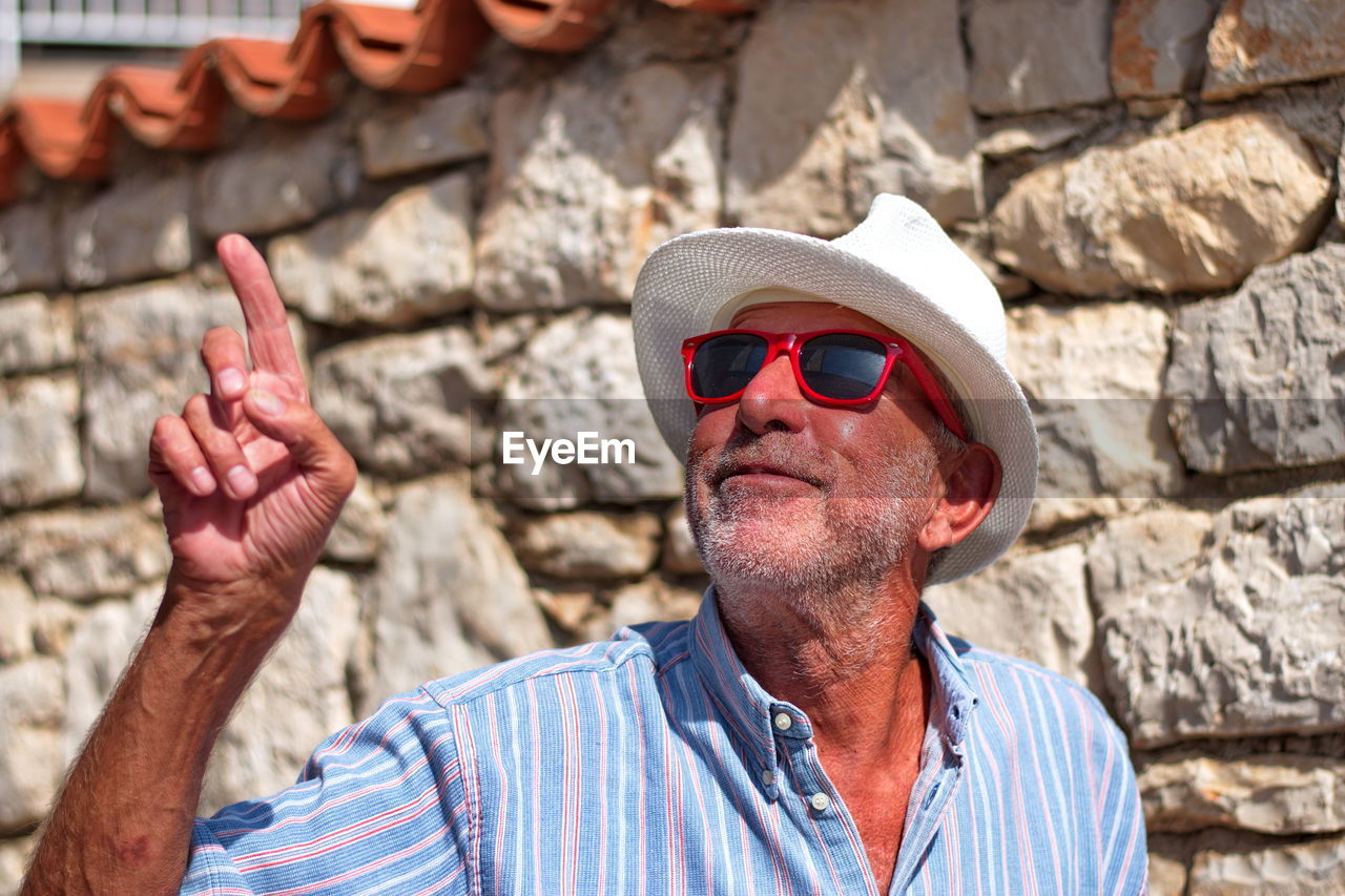 Man pointing while wearing sunglasses against wall