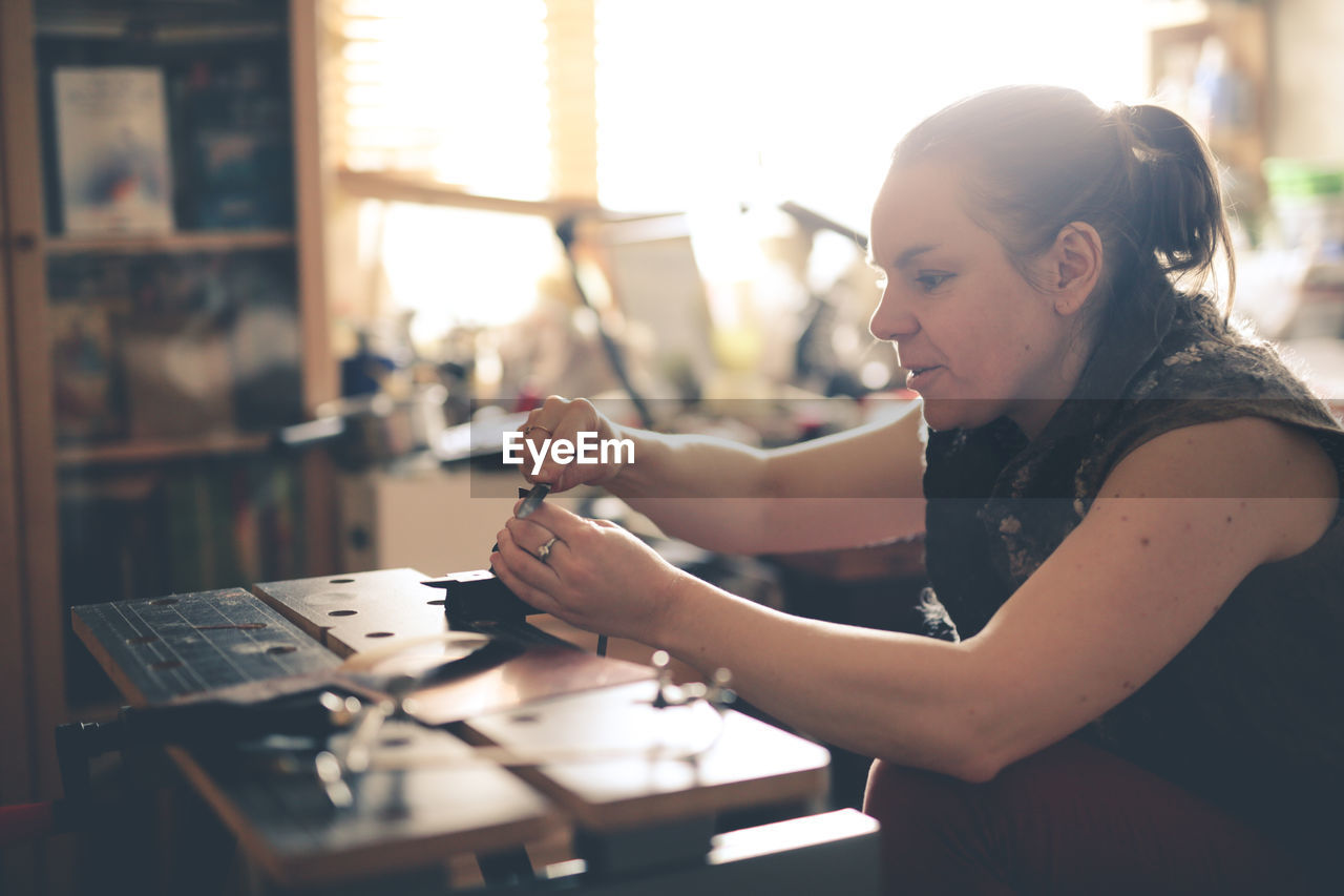 Girl master processes the metal copper plate on the workbench in the home workshop, soft focus 