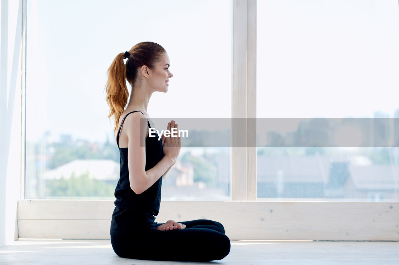 SIDE VIEW OF WOMAN SITTING ON WINDOW