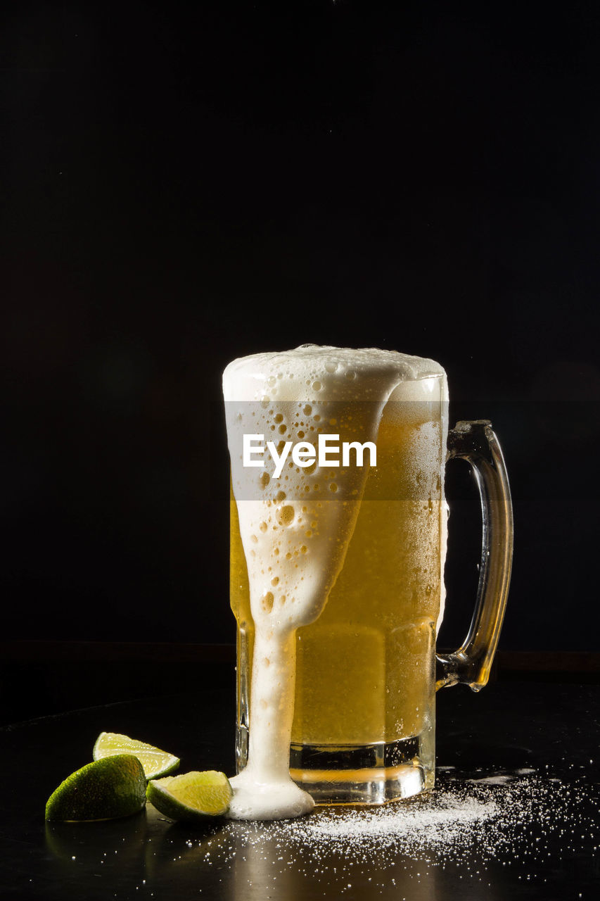 Beer spilling from glass on table against black background