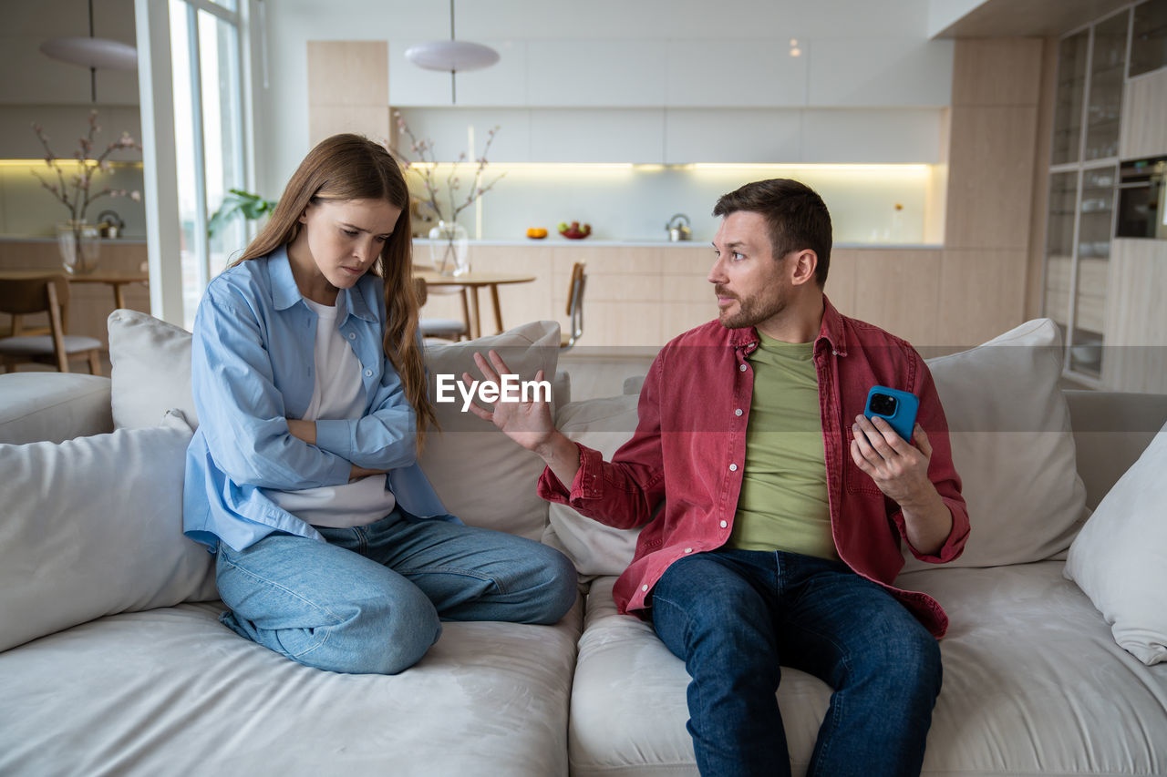 portrait of young woman using phone while sitting on sofa at home