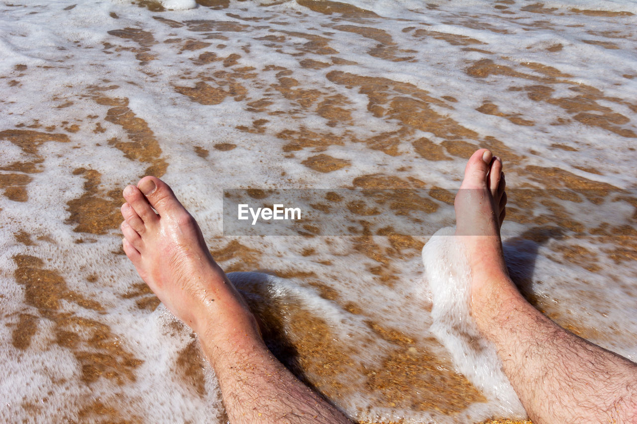 Men's legs on a sandy beach in the sea waves