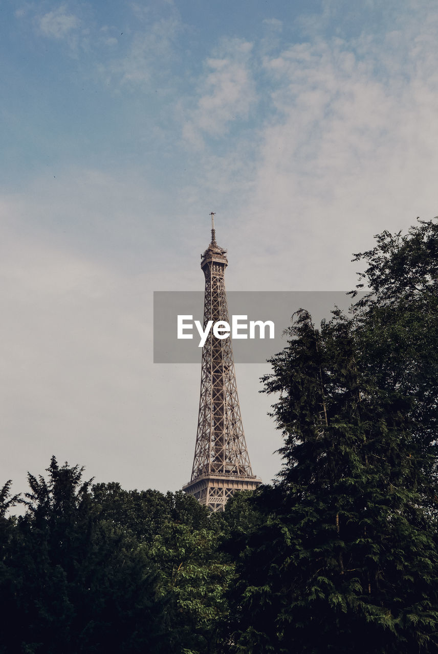 Low angle view of trees with eiffel tower in background against cloudy sky