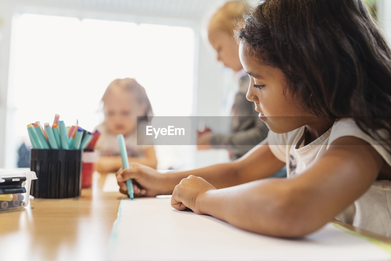 Girl using felt tip pen in drawing class with classmates in background