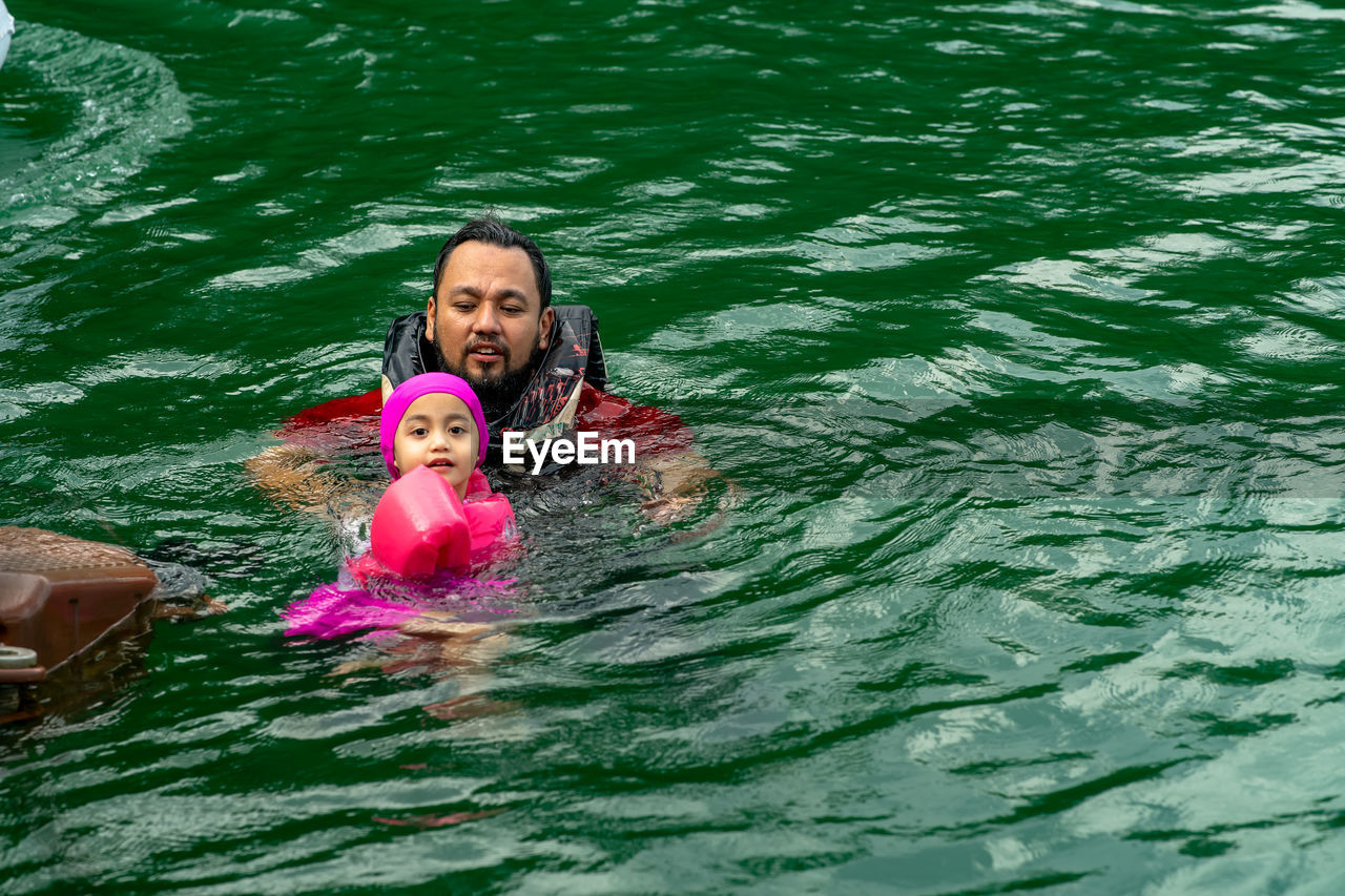 High angle view of father and daughter swimming in lake