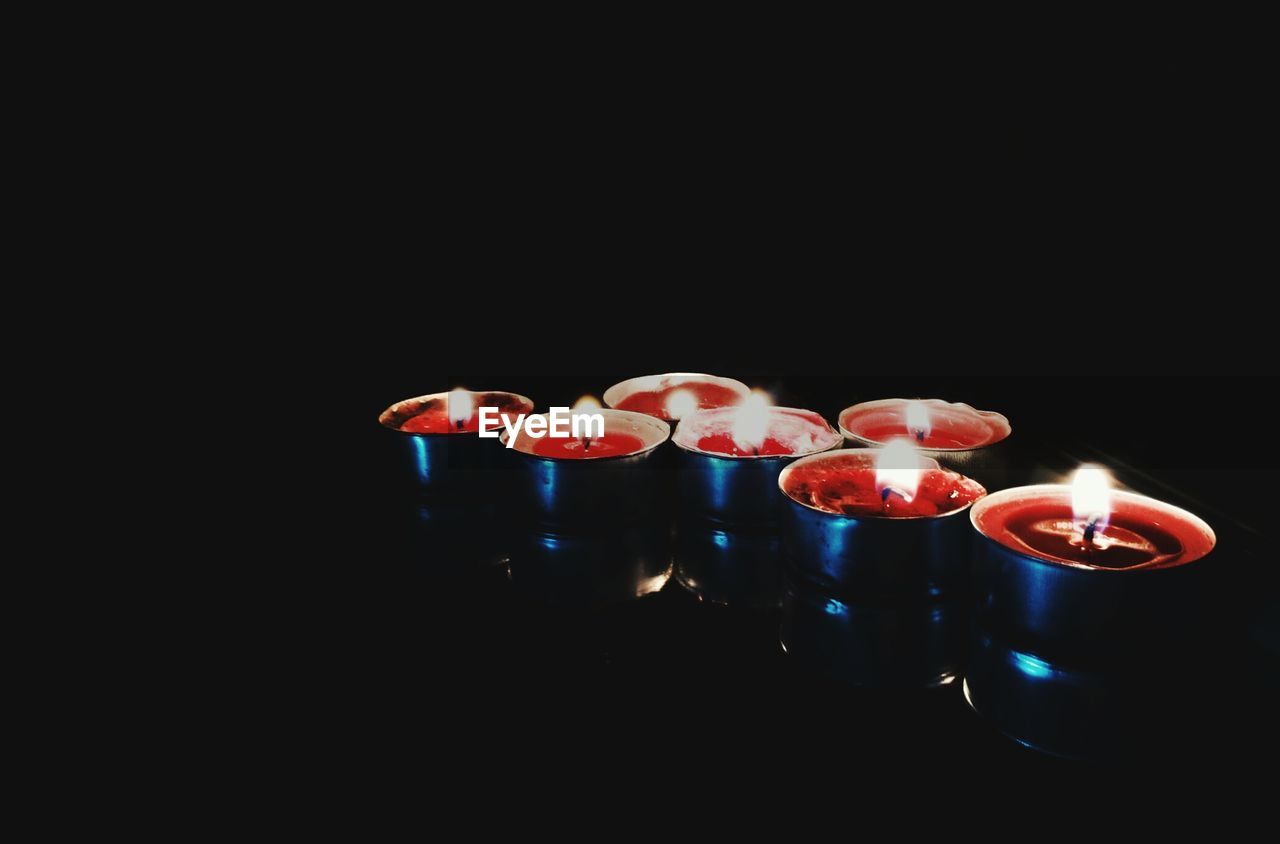 Illuminated tea light candles over black background