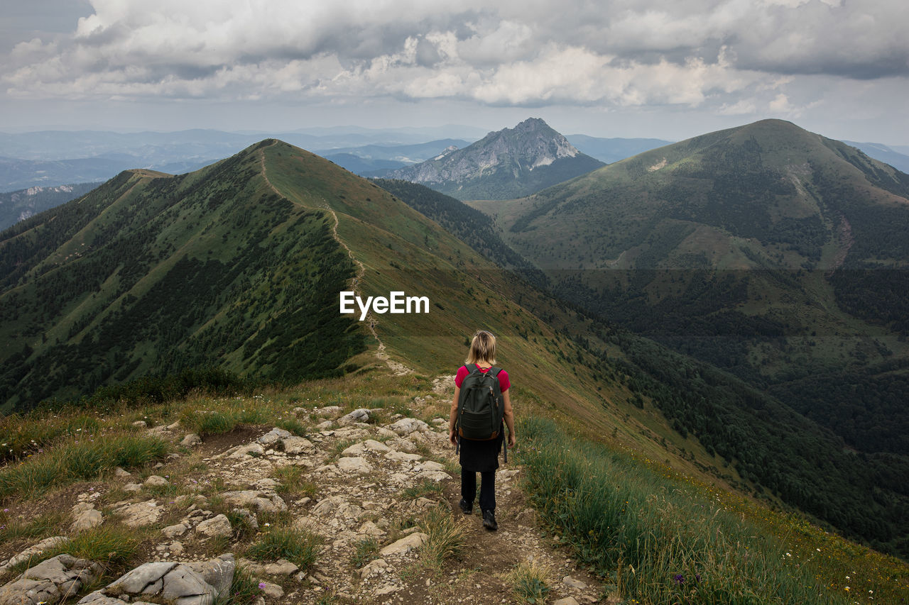 REAR VIEW OF MAN LOOKING AT MOUNTAIN RANGE AGAINST SKY