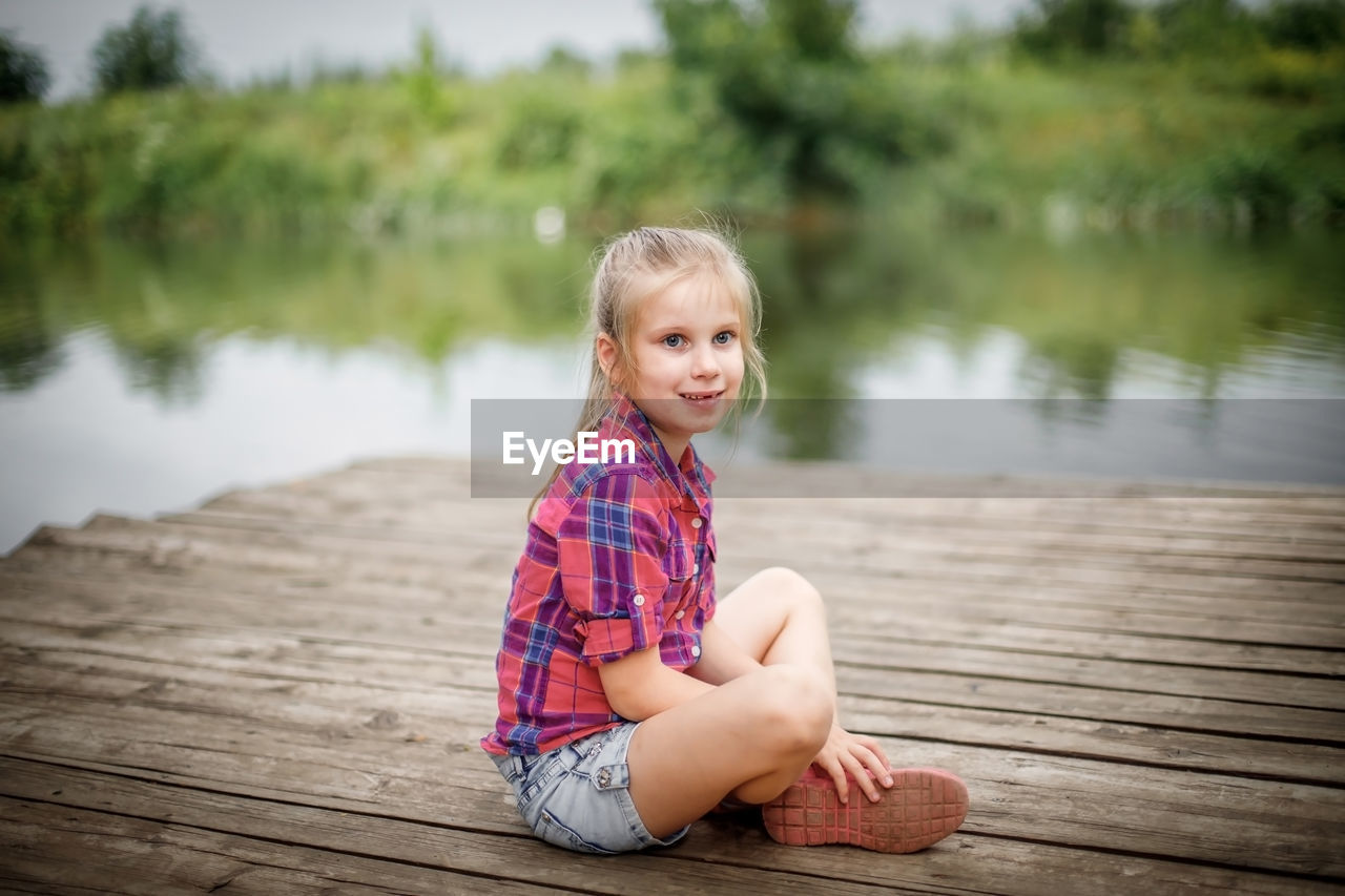 portrait of cute girl sitting on pier over lake