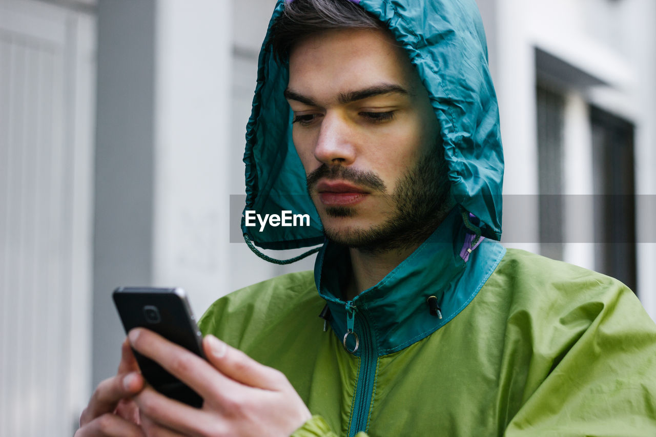 Close-up of man using phone while wearing raincoat