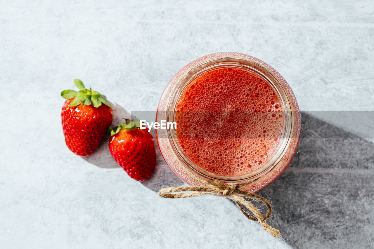 Top view of appetizing refreshing strawberry drink served in glass jar with twine on gray surface with whole berries placed nearby