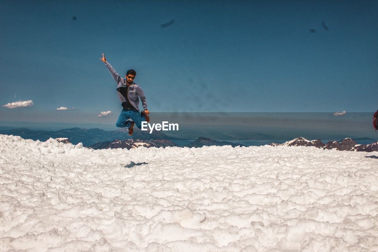 Full length of man jumping on snow against blue sky