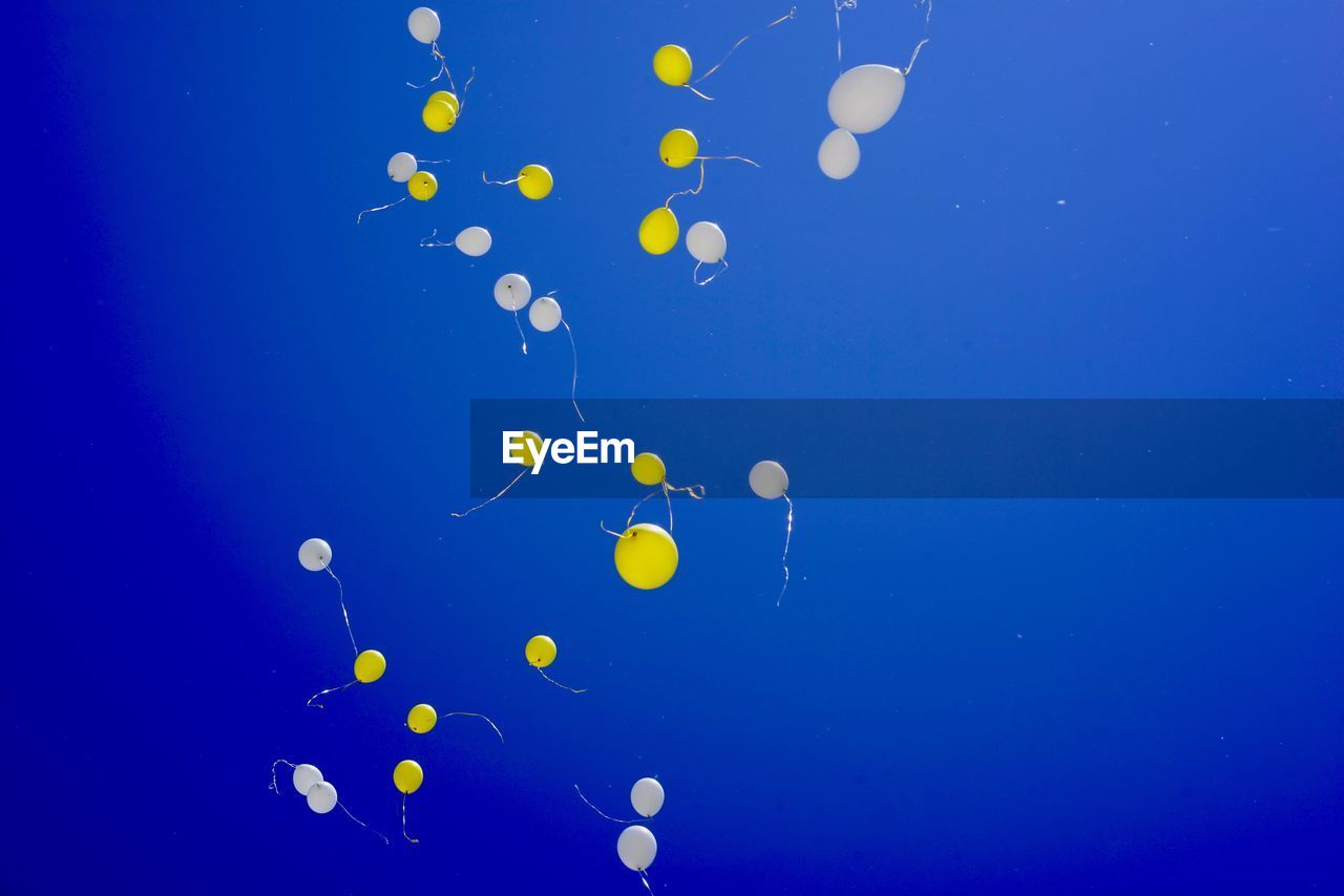 Low angle view of balloons flying against clear blue sky during sunny day