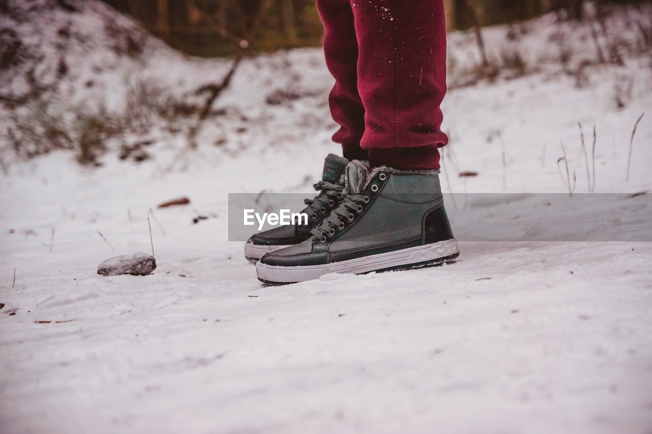 winter, footwear, low section, human leg, snow, red, one person, shoe, limb, human limb, cold temperature, spring, white, nature, leisure activity, lifestyles, winter sports, sports, adult, day, selective focus, black, human foot, standing, clothing, outdoors, land, motion, freezing, walking