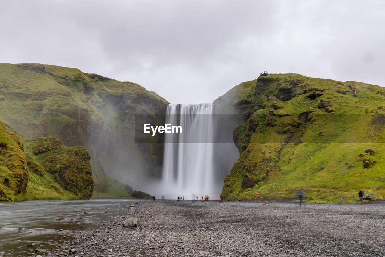 Scenic view of waterfall against cloudy sky - skogafoss