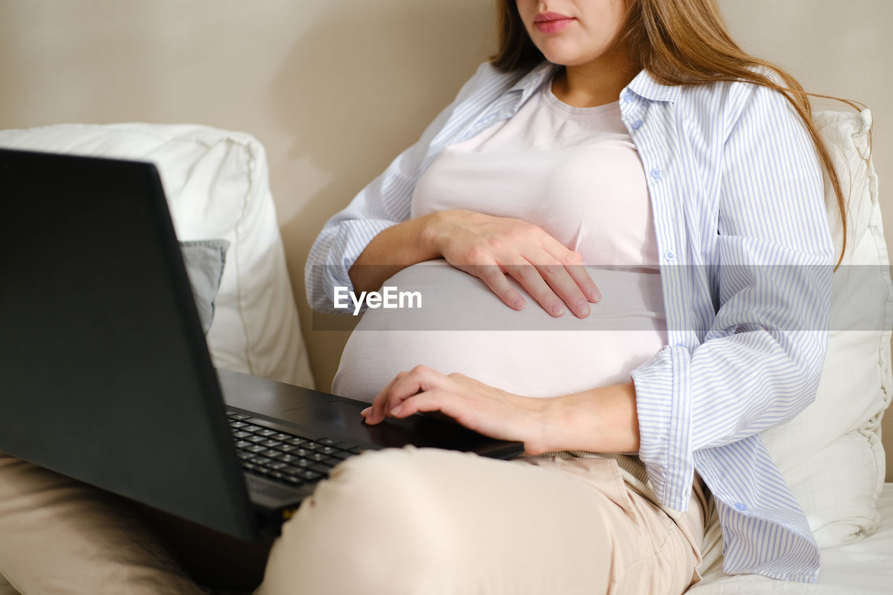 midsection of woman using laptop while sitting on bed at home