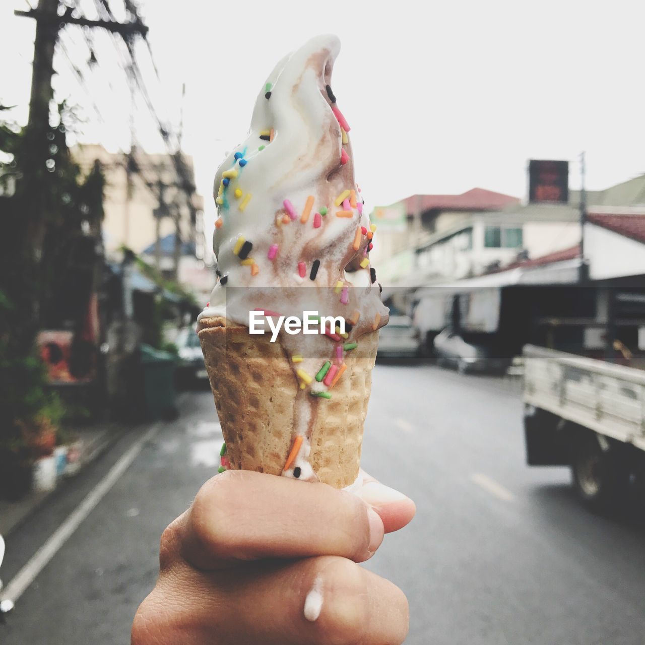 CLOSE-UP OF HAND HOLDING ICE CREAM CONE AGAINST THE SKY