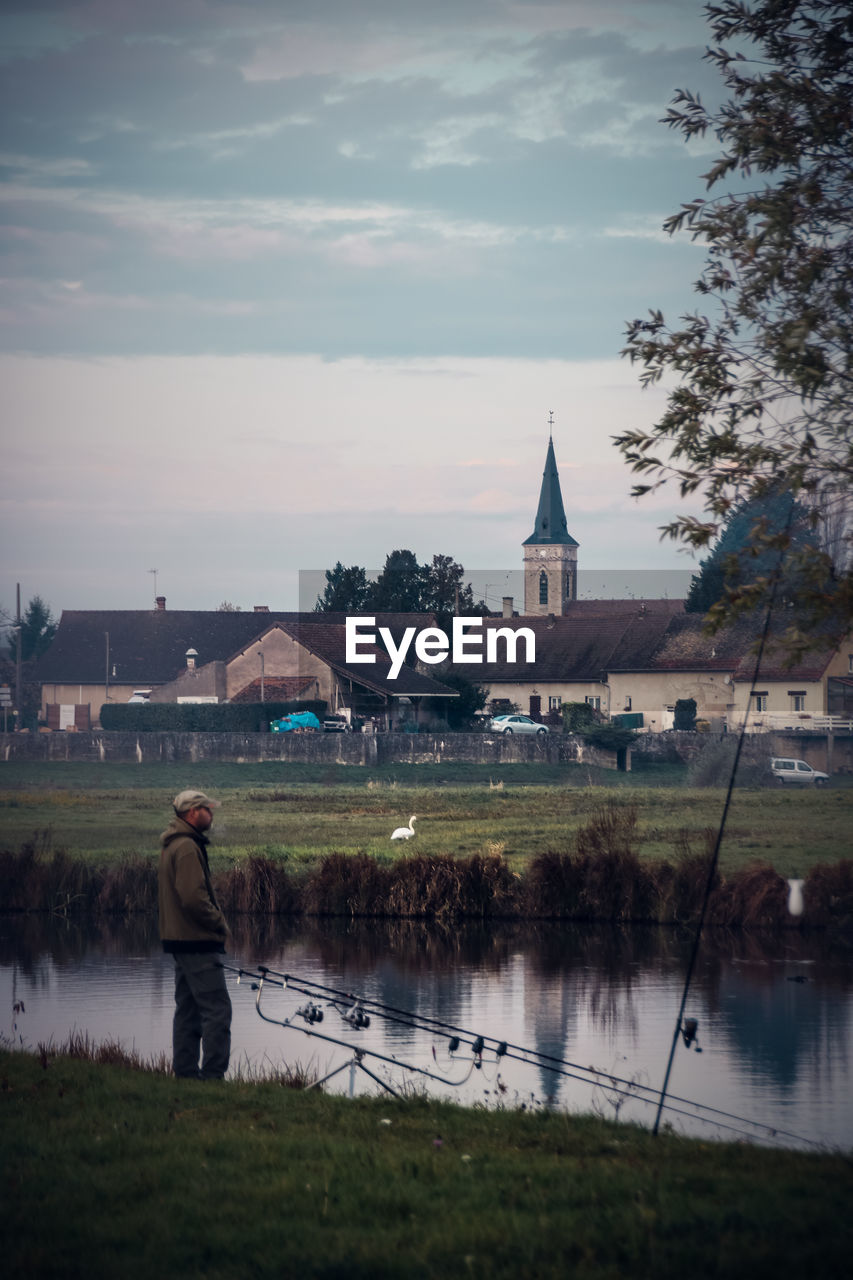 Side view of man fishing by lake against church