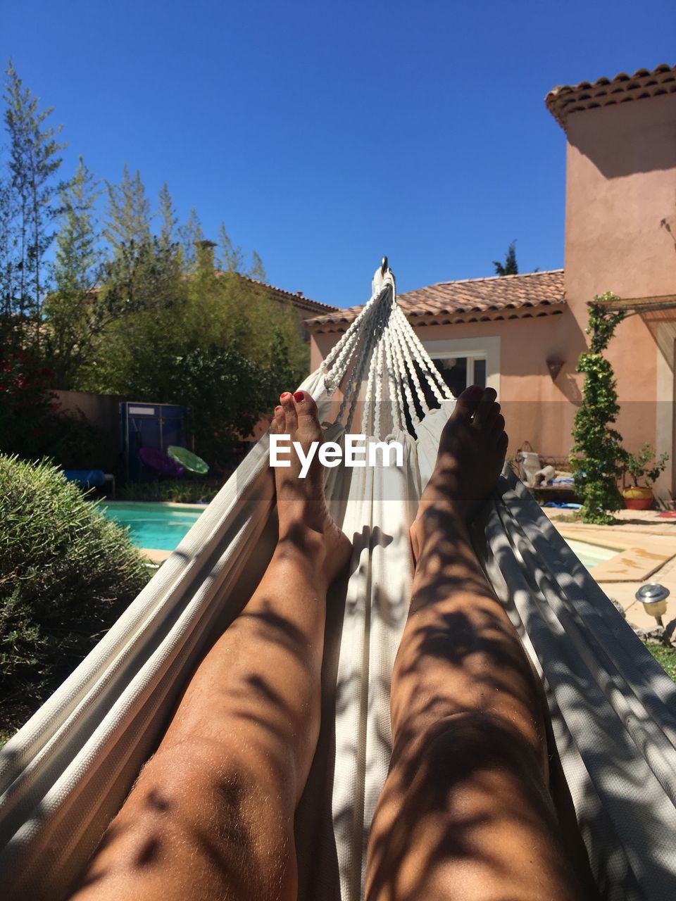 Low section of woman resting on hammock in yard against clear blue sky