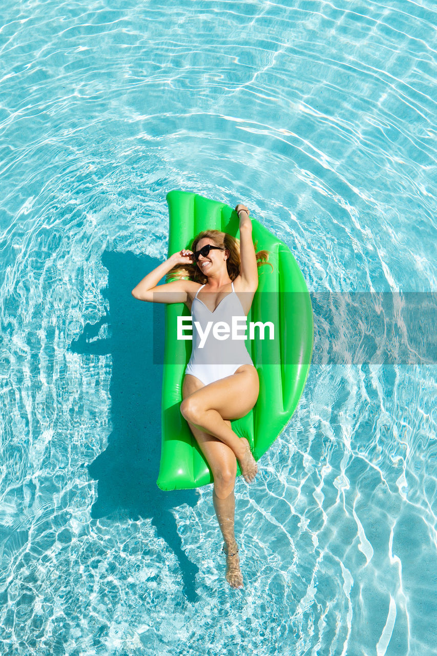 From above full body smiling female in white one piece suit chilling on air mattress on pool water on hot sunny day