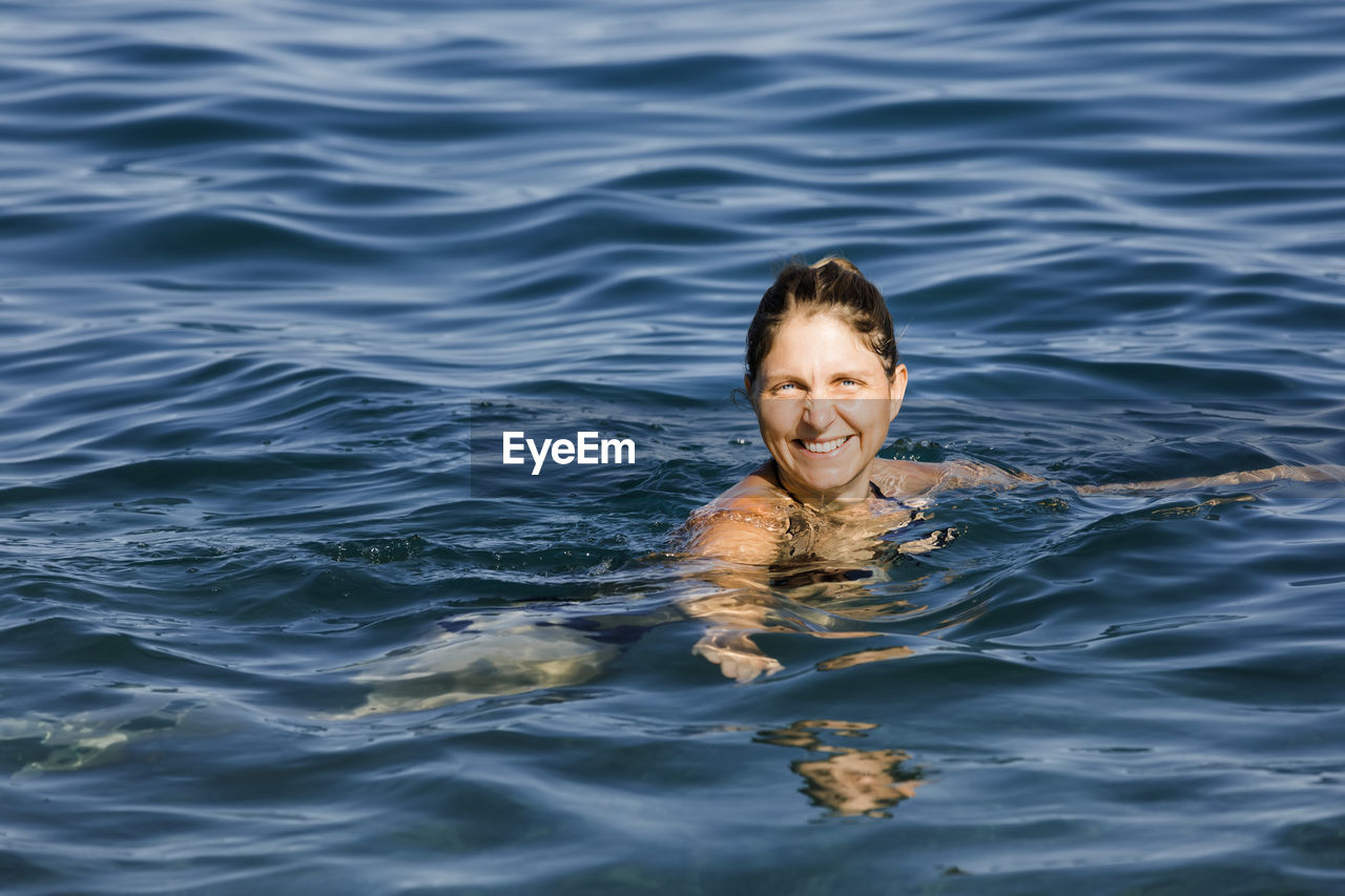 PORTRAIT OF A SMILING YOUNG MAN SWIMMING IN SEA