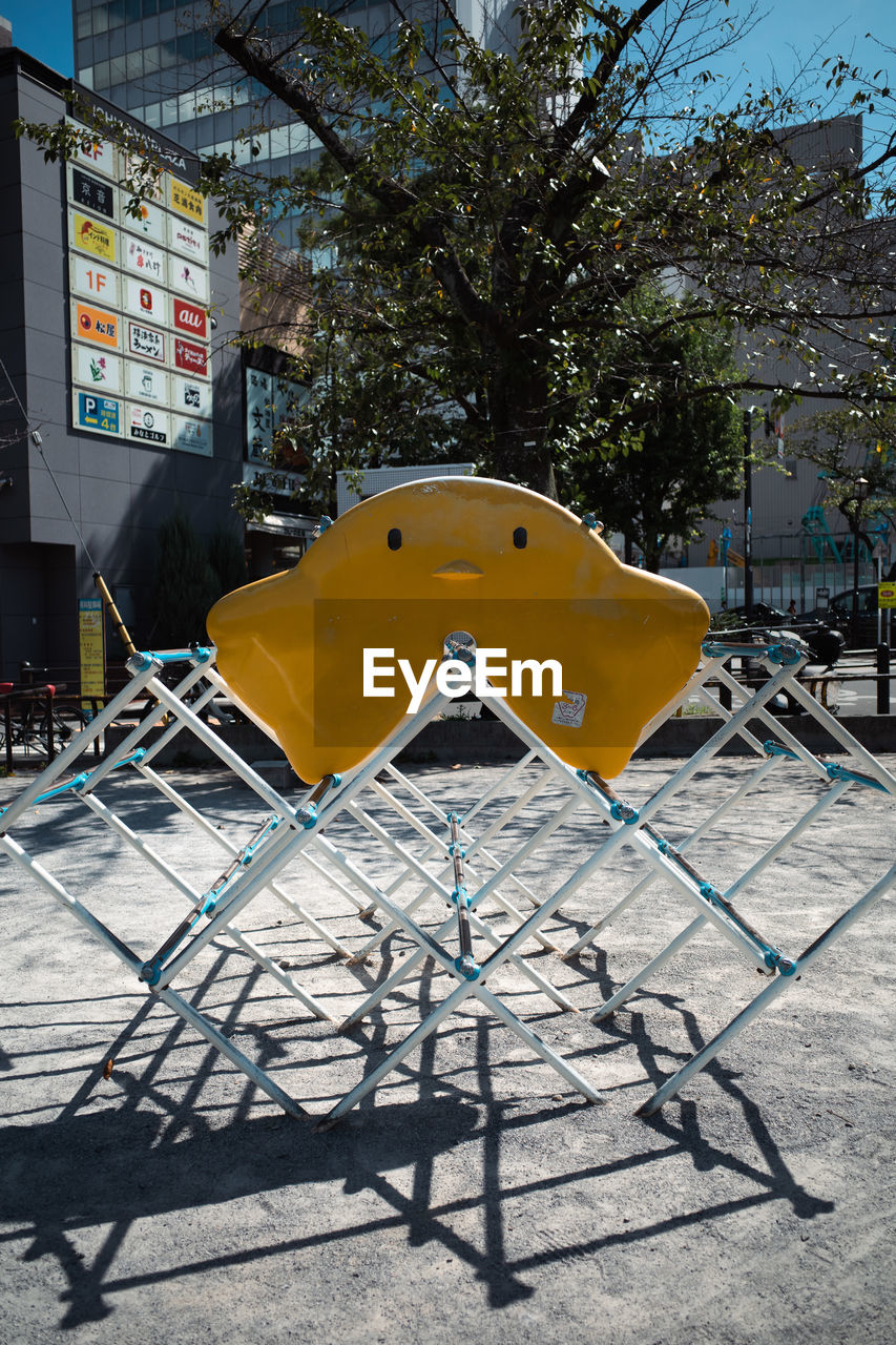 architecture, playground, nature, tree, city, built structure, no people, day, shadow, building exterior, plant, sunlight, urban area, outdoors, chair, street, seat, sign