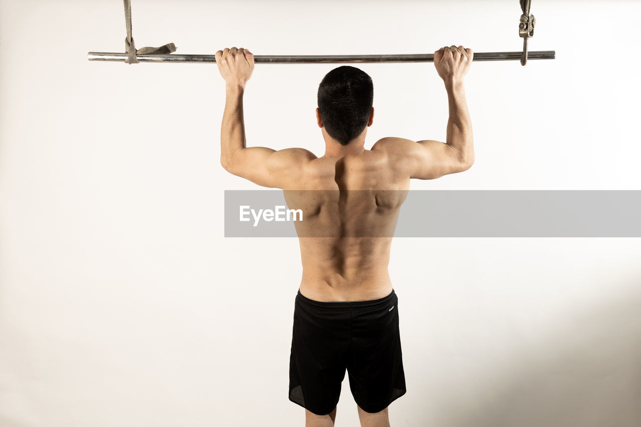REAR VIEW OF SHIRTLESS MAN AGAINST WHITE BACKGROUND