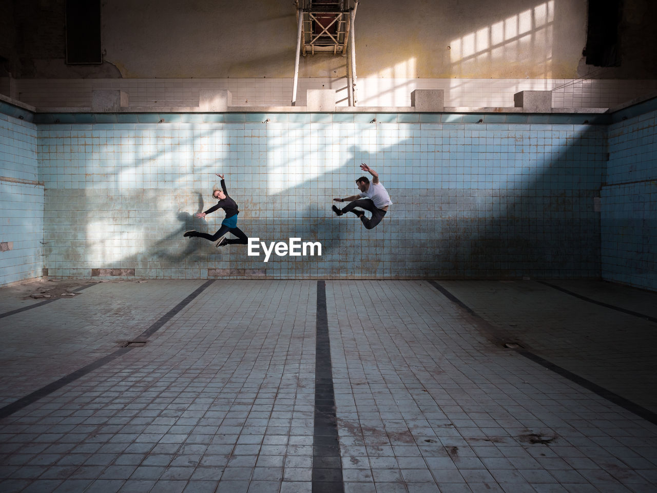 Friends jumping in abandoned empty swimming pool