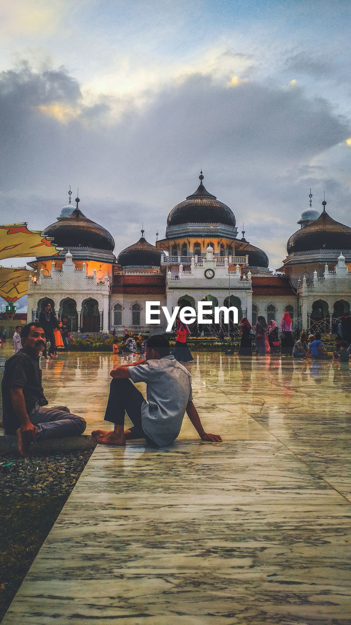 PEOPLE SITTING OUTSIDE TEMPLE AGAINST SKY