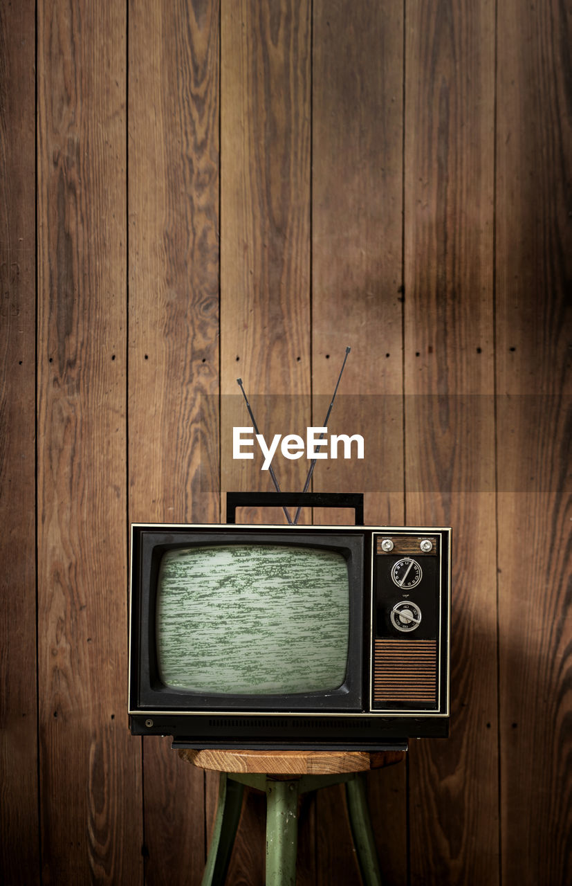 Old television set on stool against wooden wall