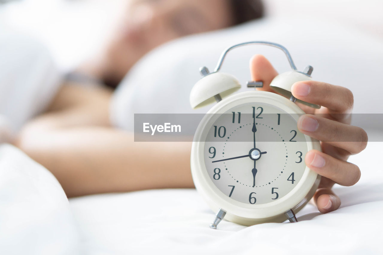 Woman with alarm clock sleeping on bed