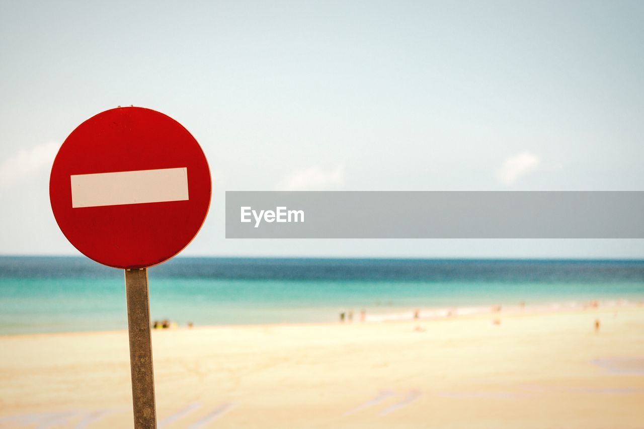 Close-up of do not enter sign at beach against sky