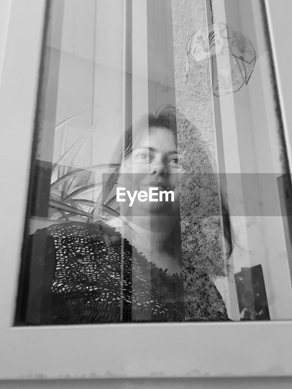 PORTRAIT OF WOMAN LOOKING THROUGH GLASS WINDOW
