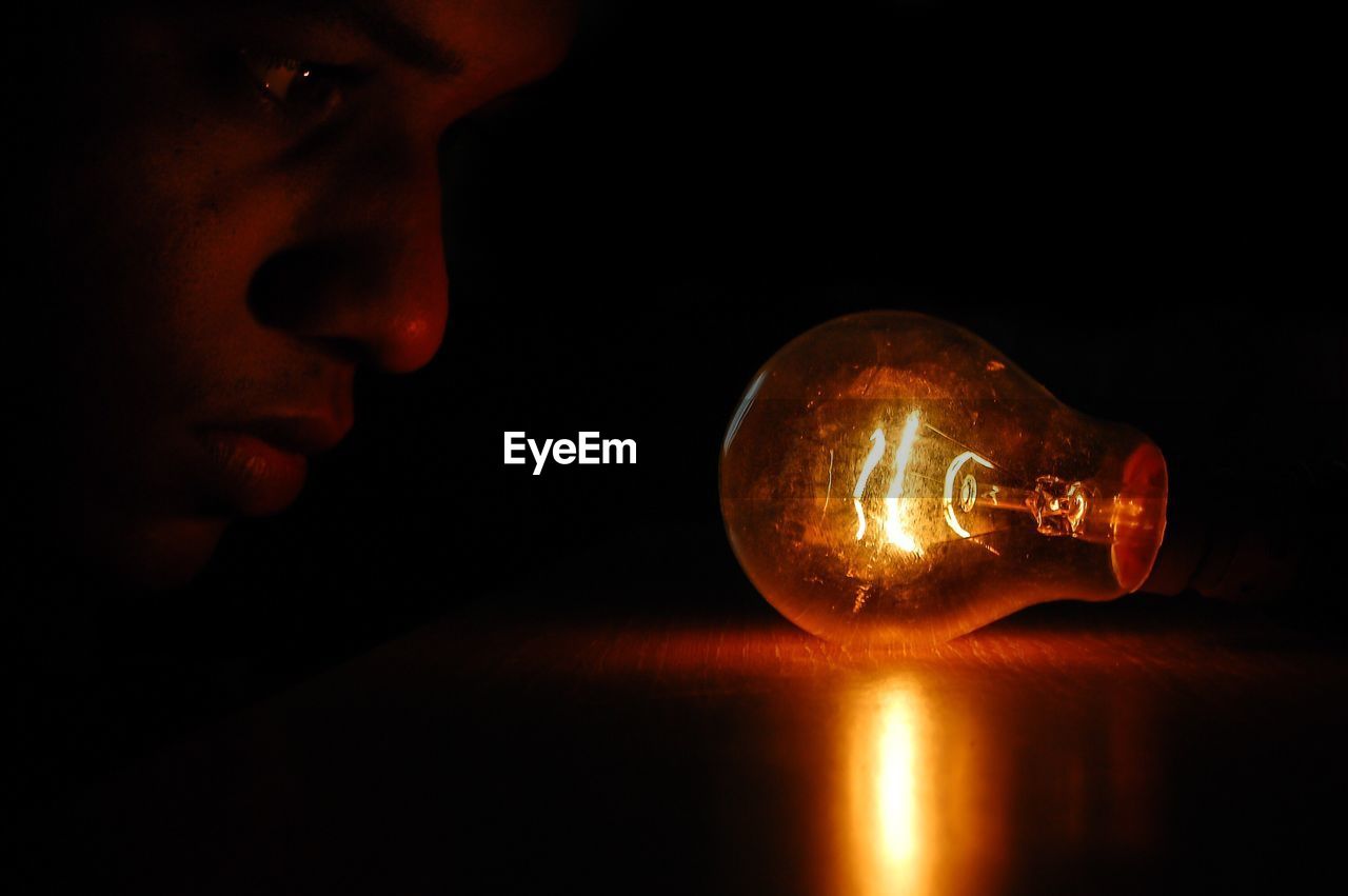 Close-up of man looking at illuminated light bulb