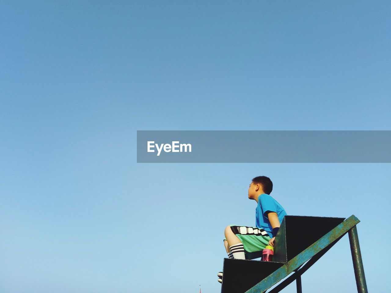 Low angle view of boy sitting on steps against blue sky