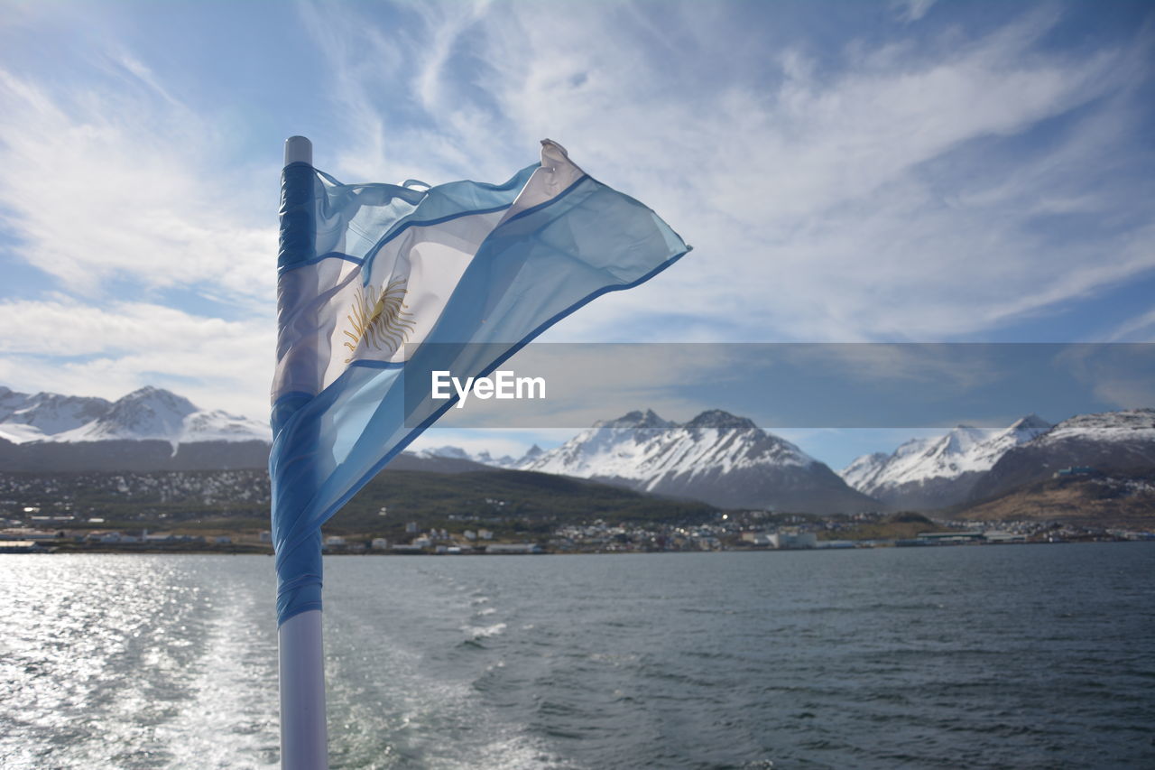 Argentinian flag by sea and snow covered mountains against sky