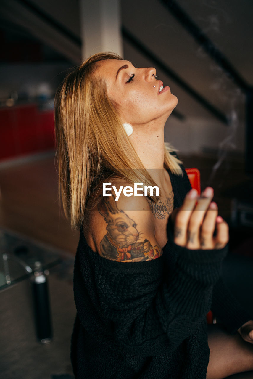 Young tattooed woman smoking and relaxing in her room.